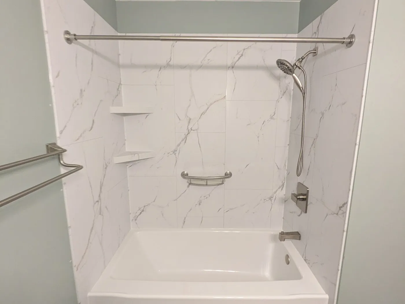 Rebuilt tub alcove with a white marble-look surround, level corner shelves and a new shower system