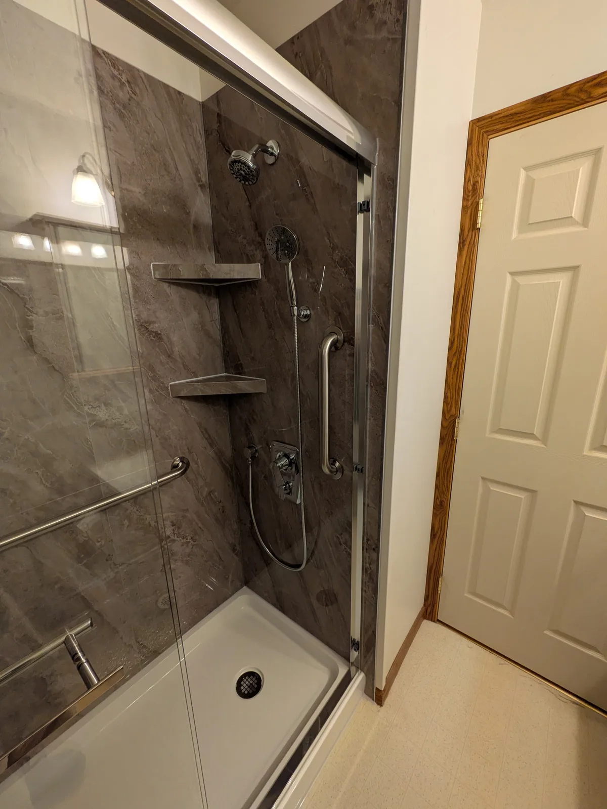 Finished walk-in shower with a handheld shower and chrome grab bar