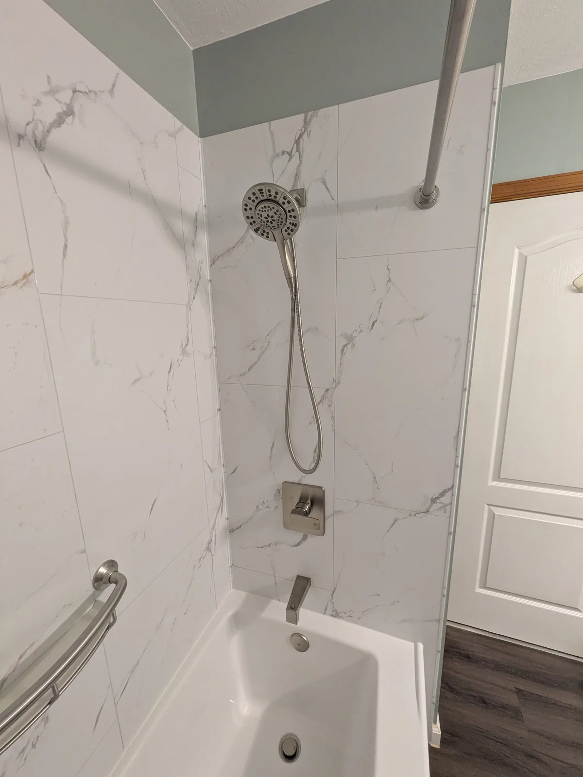 Remodeled tub and shower with white marble-look walls, handheld shower and a grab bar