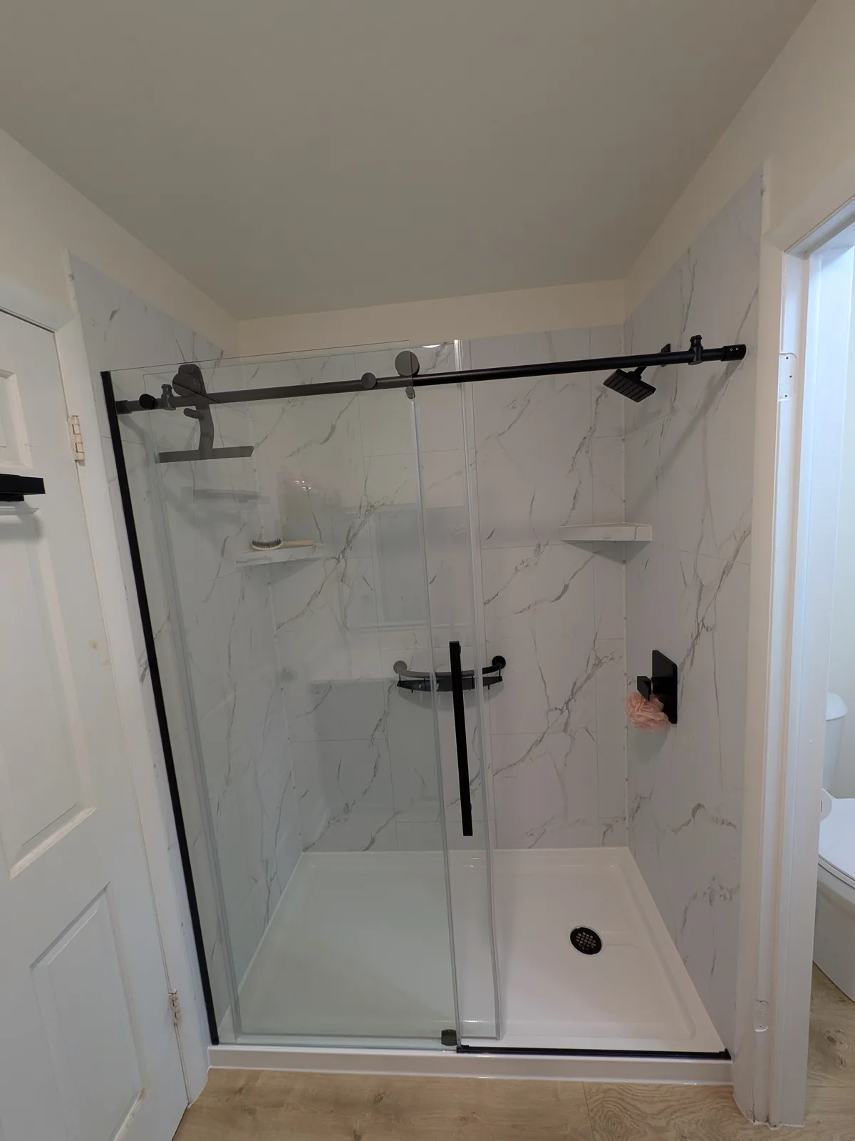 Walk-in shower in white marble-look panels with black sliding glass doors and a low-threshold base