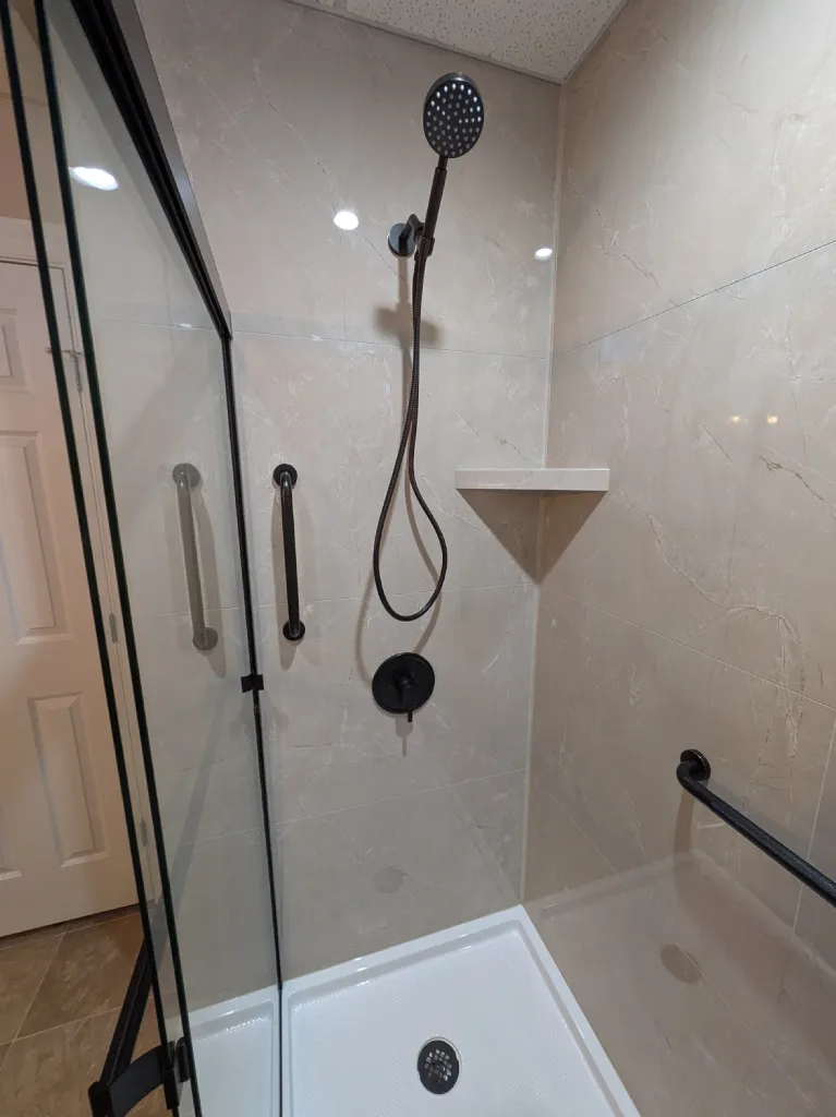 Handheld shower on its bracket above a bronze mixer valve, with grab bars either side of the tiled shower wall