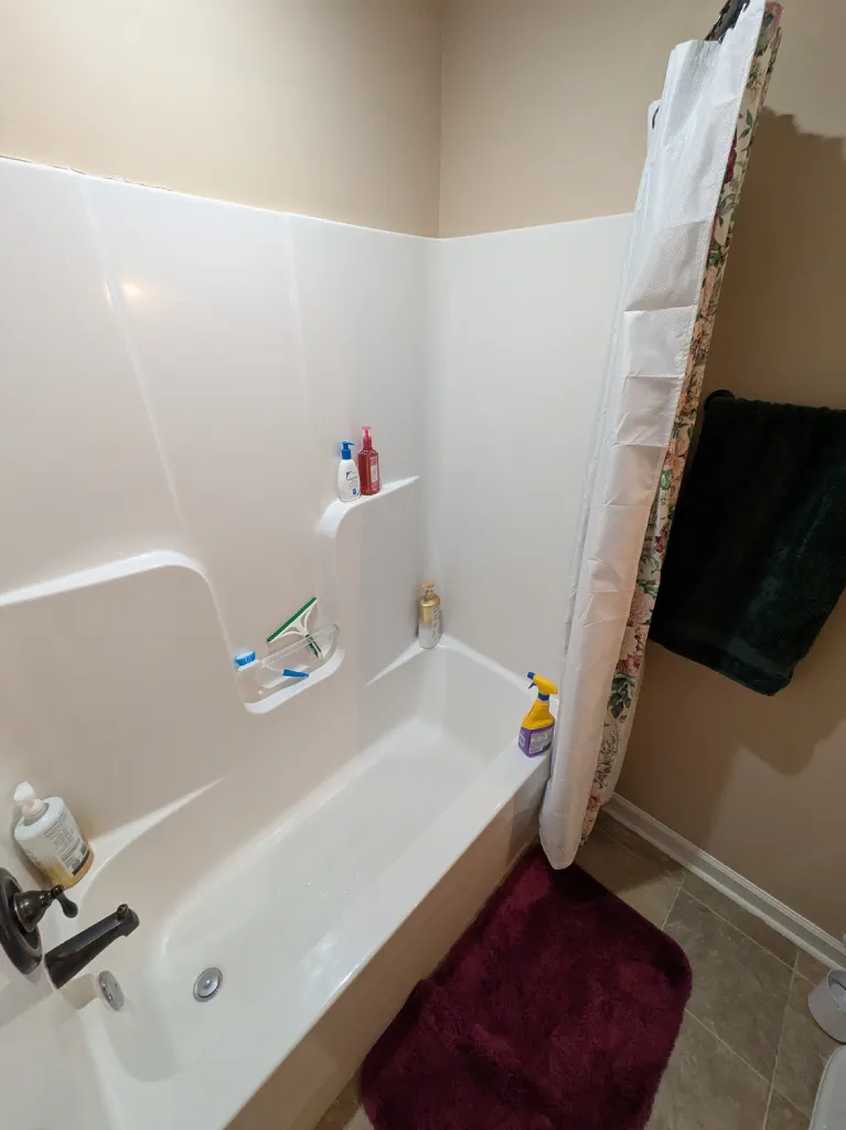 The old tub from the left, shower curtain drawn back against the beige wall