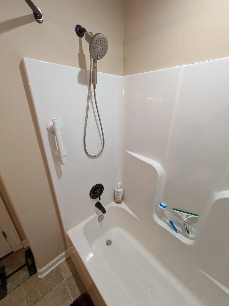 The old surround with its moulded shelves, handheld shower and white grab bar before removal