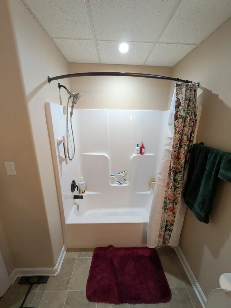 The old tub alcove from the doorway, floral curtain drawn across it under a drop ceiling
