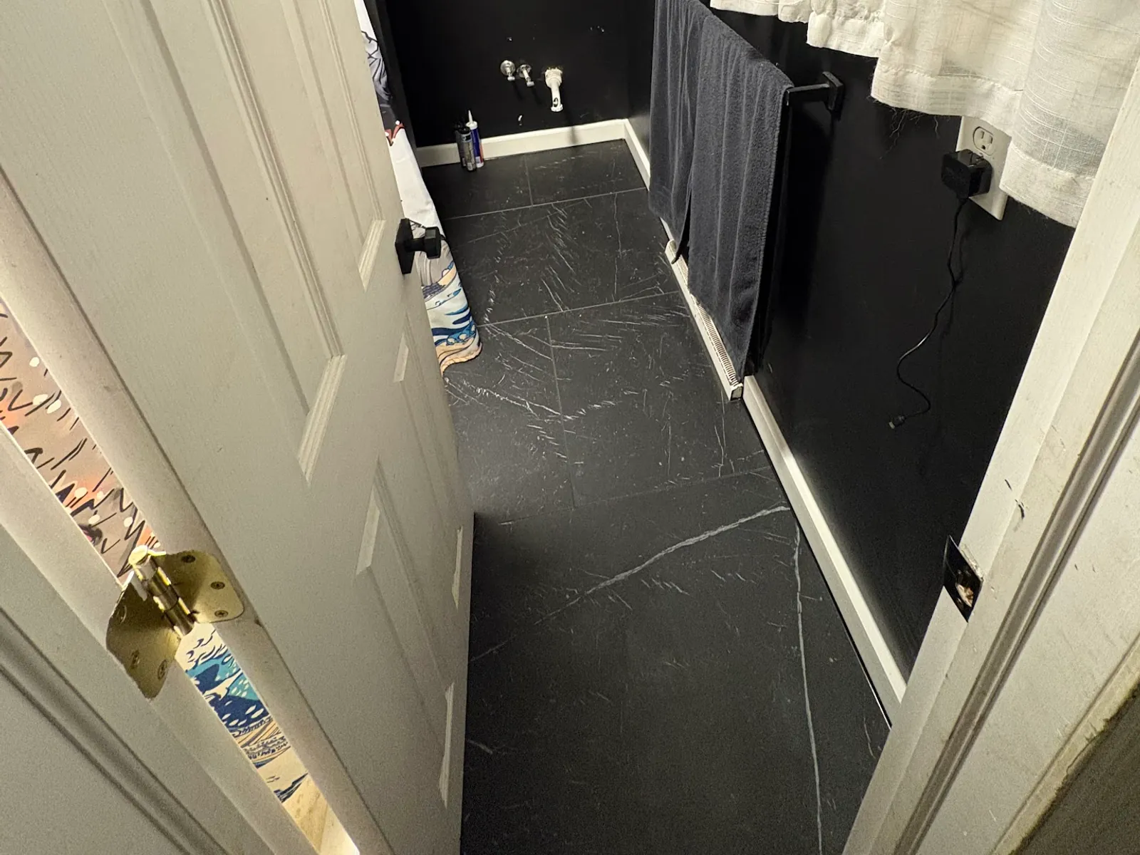 Powder room floored and walled in black marble-look tile with matte black fittings