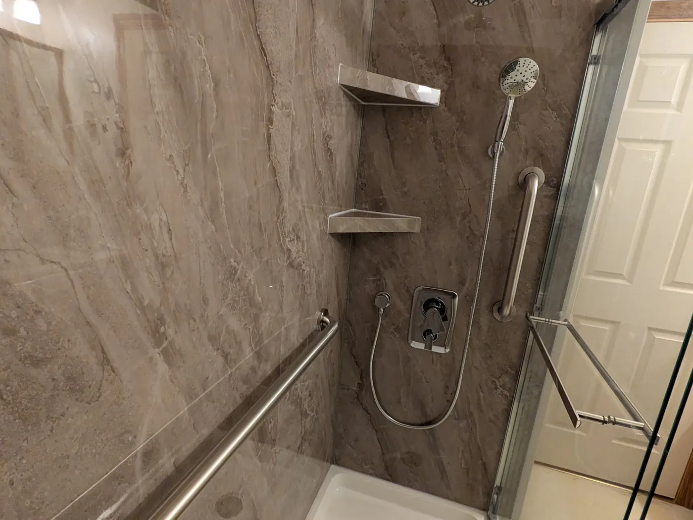 Finished shower lined in stone-look panels, with a handheld system, grab bar and glass door